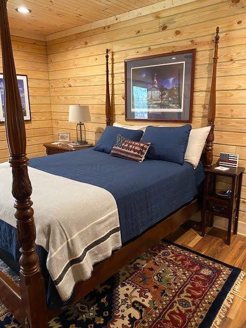Cozy bedroom with a wooden four-poster bed, blue bedding, and rustic wood-paneled walls.