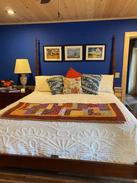 A cozy bed with colorful pillows and quilt against a blue wall with three framed pictures above.