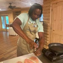 A man in an apron seasons raw salmon fillets in a cozy wooden kitchen.