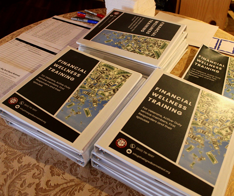 Stacks of binders labeled Financial Wellness Training on a table with pens and sign-in sheets.