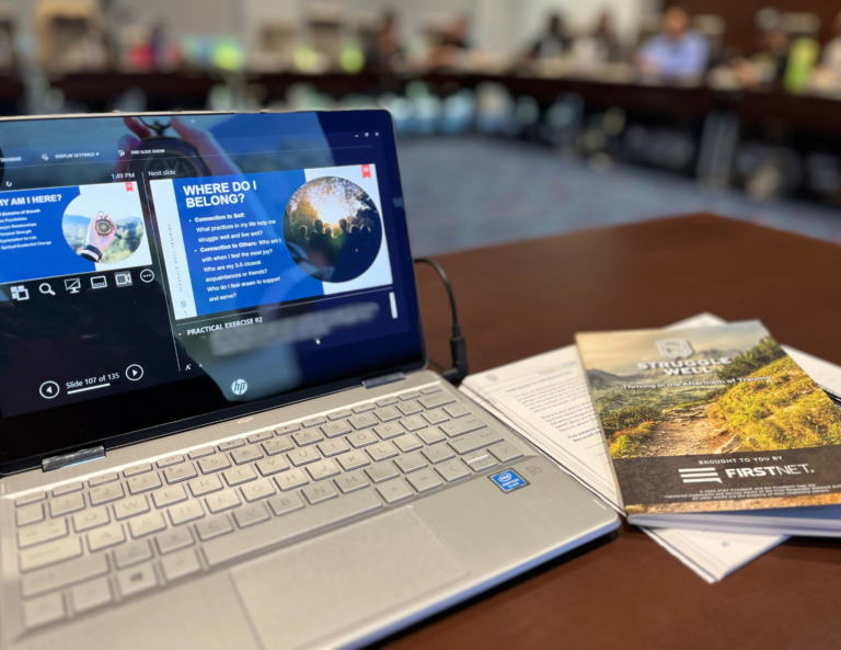 Open laptop showing a presentation, with a booklet titled STRUGGLE WELL on a table in a meeting room.