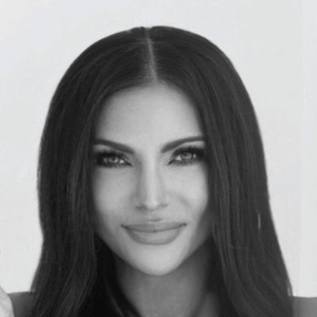 A woman with long, dark hair and defined features looks forward, smiling softly in black and white.