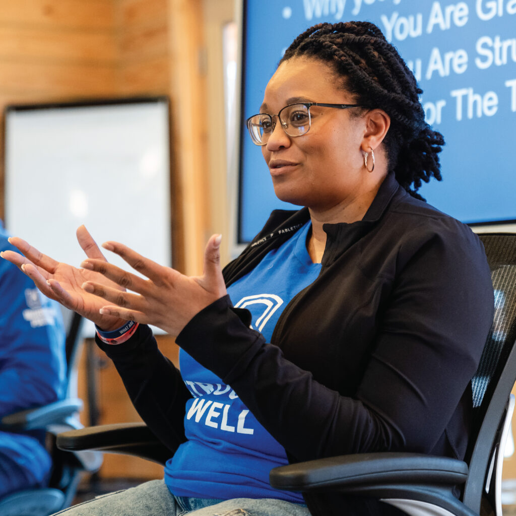 A woman speaking and gesturing with her hands during an indoor presentation or discussion.
