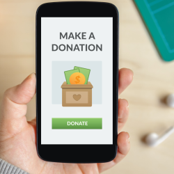 A hand holds a phone displaying a Make a Donation screen with a donate button and money icon.