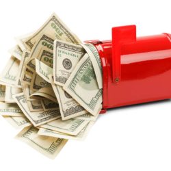 Red mailbox tipped over with lots of US dollar bills spilling out onto a white surface.